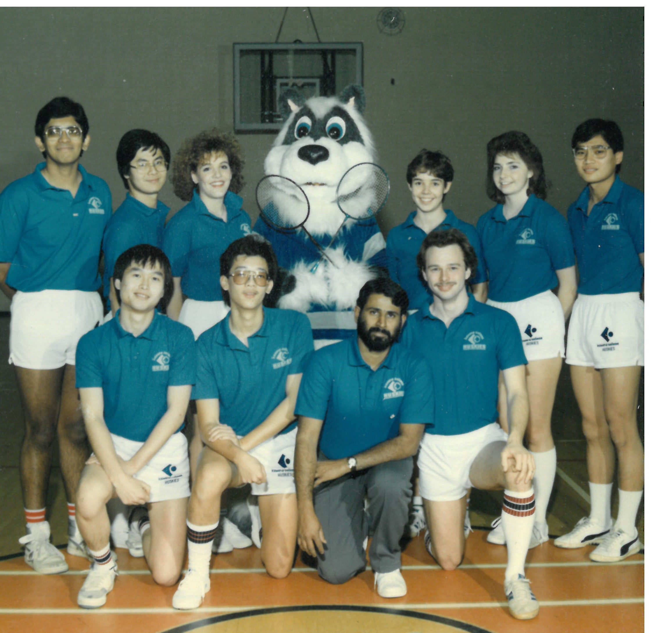 student badminton athletes posing in a gym with huskies mascot