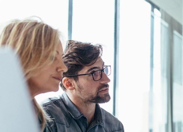 a man and woman listening to someone off camera in business clothes. 