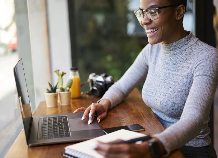 business woman smiling writing on notepad looking at laptop