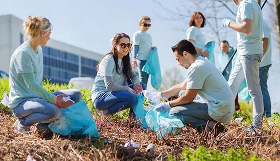 group of people picking up garbage outside holding garbage cans