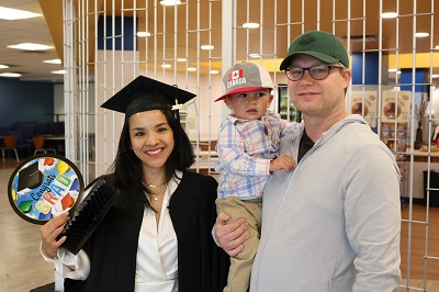 student graduating from LINC program in cap and gown smiling with husband and son