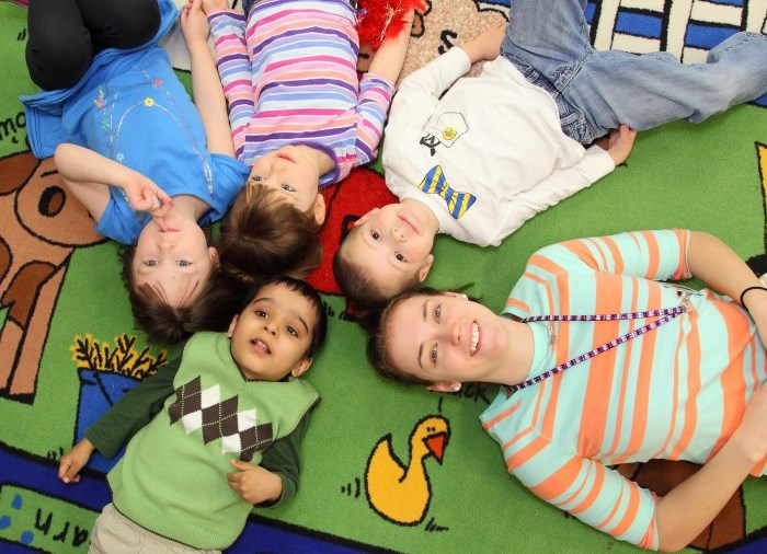 early childhood worker laying on colourful mat with children