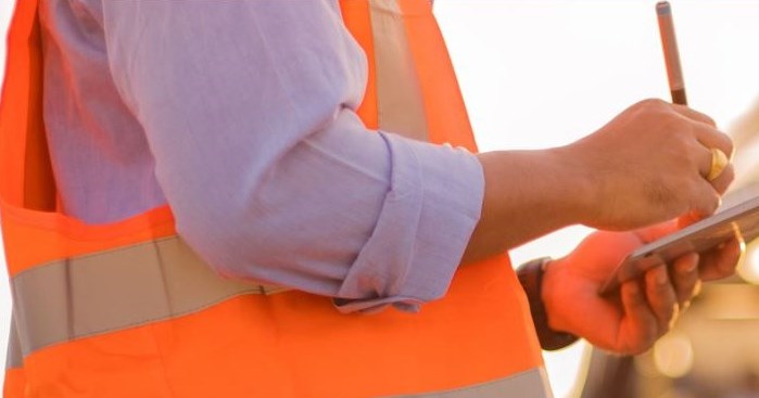 man wearing safety vest with clipboard writing on it