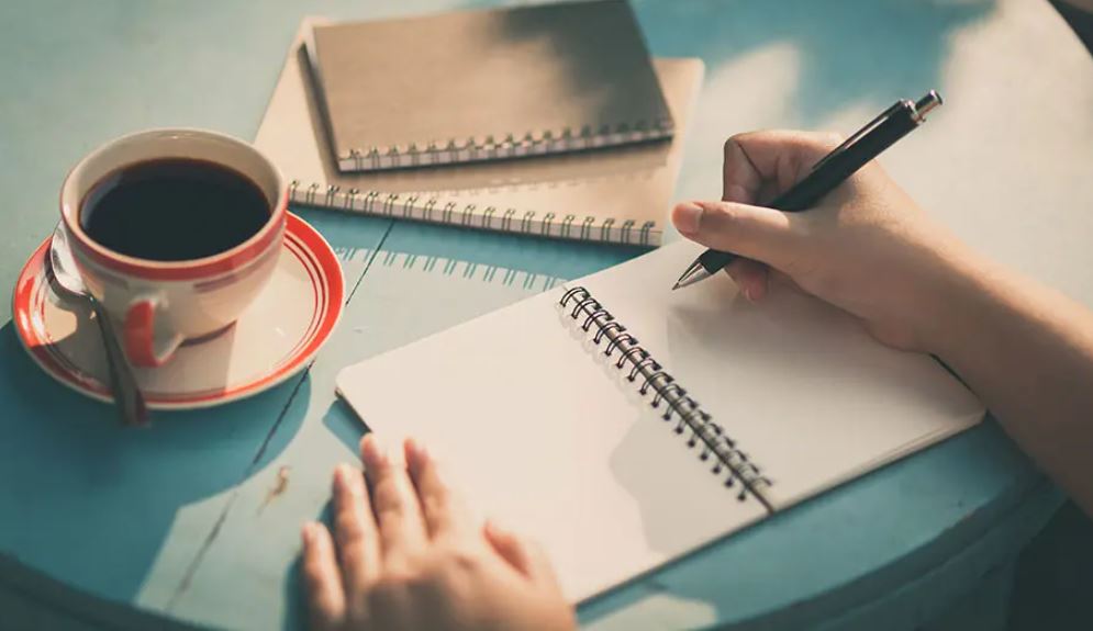 two hands writing on a notepad with a pen