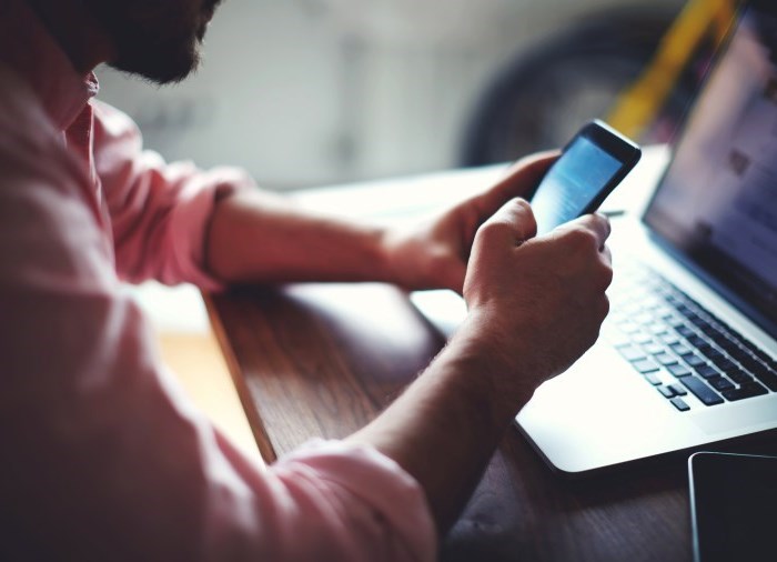 man holding a cell phone in front of a laptop