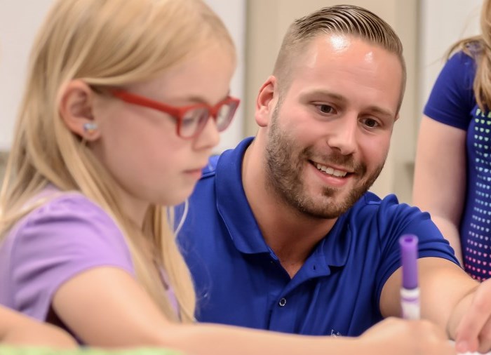 male teacher helping young child student with school work smiling.