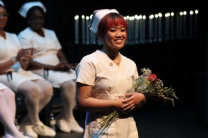student nurse in white nursing uniform holding flowers on stage after receiving her nursing pin