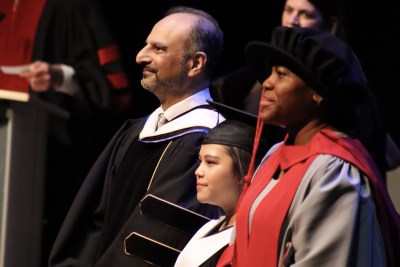 graduate standing with college president and vice president on stage during convocation