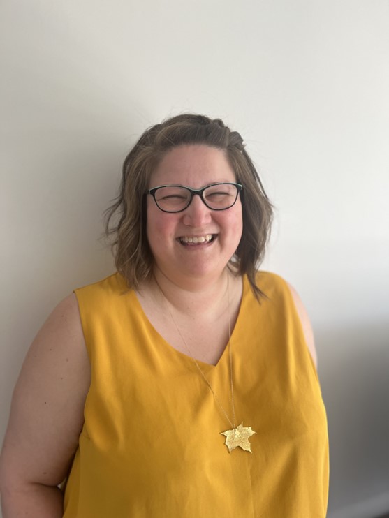 smiling woman with dark shoulder length hair and glasses wearing a yellow shirt