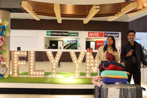 male and female international student with luggage happily smiling by the FLY YMM sign at the fort mcmurrya airport