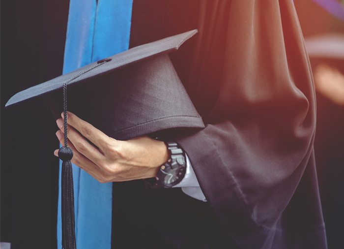 smiling young woman in graduation cap and gown celebrating