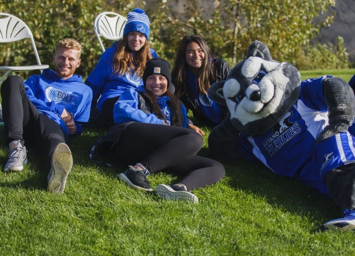 Huskies athletes sitting in the grass with Mascot KING