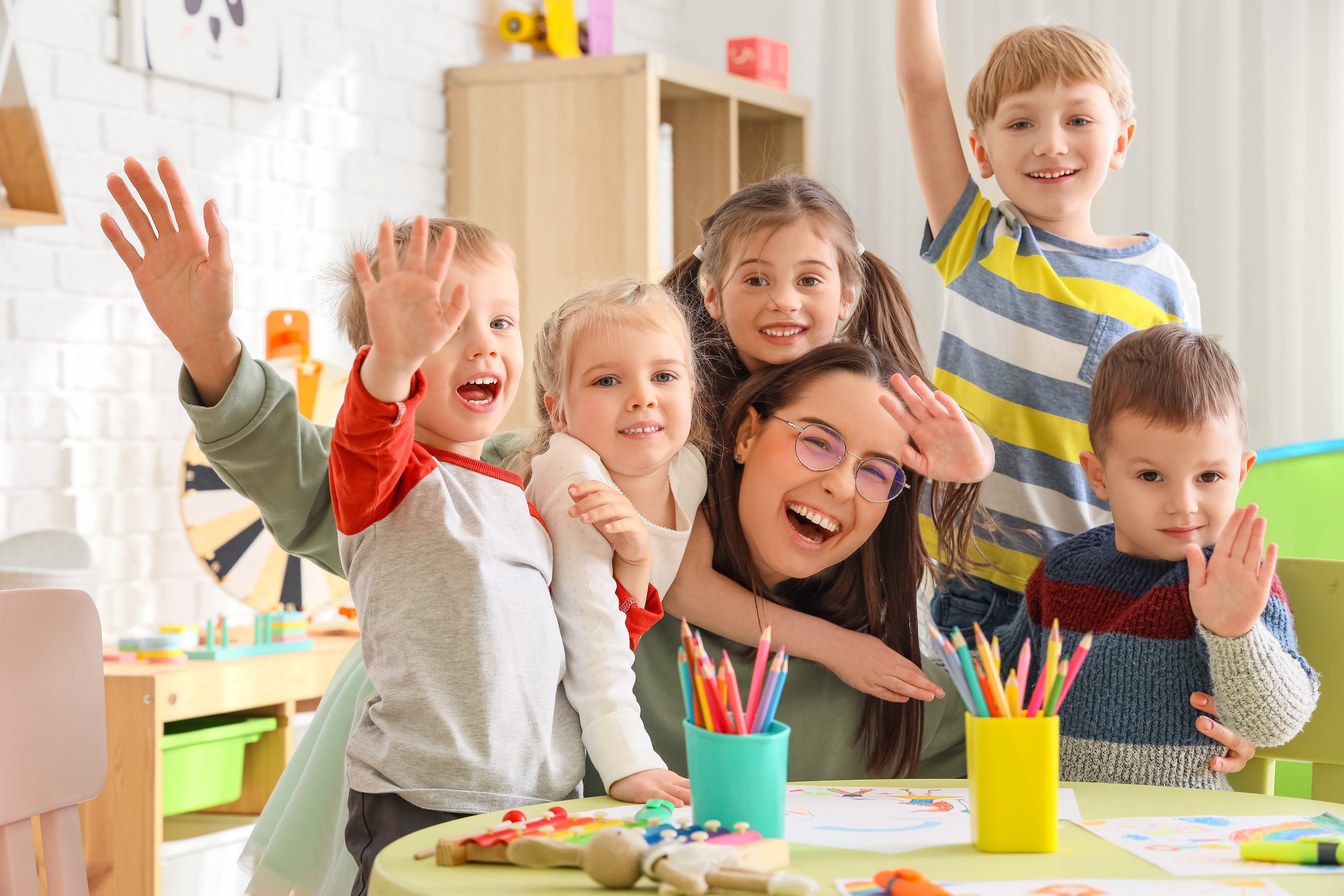 Cute little children hugging nursery teacher in kindergarten
