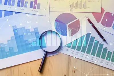 Bar graphs, charts, and business analytics documents spread across a desk with a magnifying glass and pen.