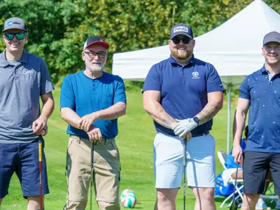 Four guys leaning on their golf clubs posing for picture