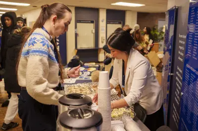 A woman leaning over a table of dessert trays while another woman stands across from her, looking down at them.