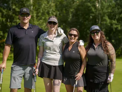 Four people posing on a golf course holding golf clubs.