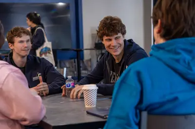Two men laughing while talking with two other students who have their backs to the camera.
