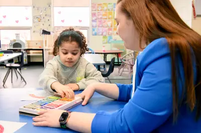 An early childhood educator helps a child choose coloured pastels during an art activity in a classroom.