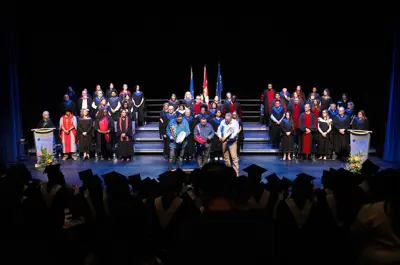 Indigenous performers playing traditional round instruments on stage during the convocation ceremony, with faculty seated behind them.