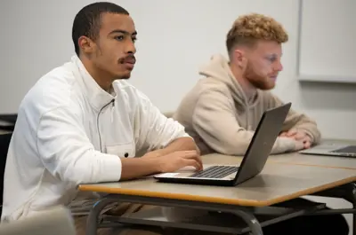 Two students in class taking notes on their laptops