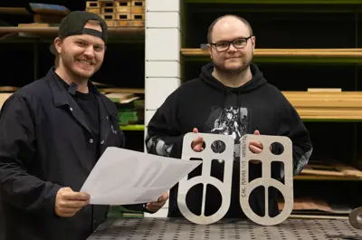 Two students in a CNC workshop holding metal cutouts and design templates created through CNC plasma cutting.
