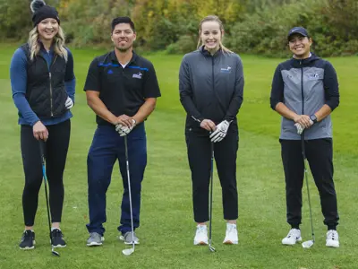 Four people holding their golf clubs posing for picture on a golf field