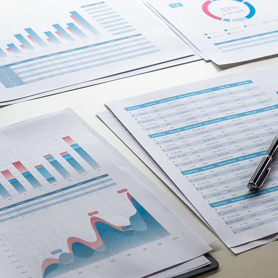 Documents displaying charts, graphs, and business reports spread across a desk beside a pen.