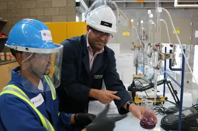 Two individuals wearing safety gear and hard hats working together in a power engineering lab with industrial testing equipment.