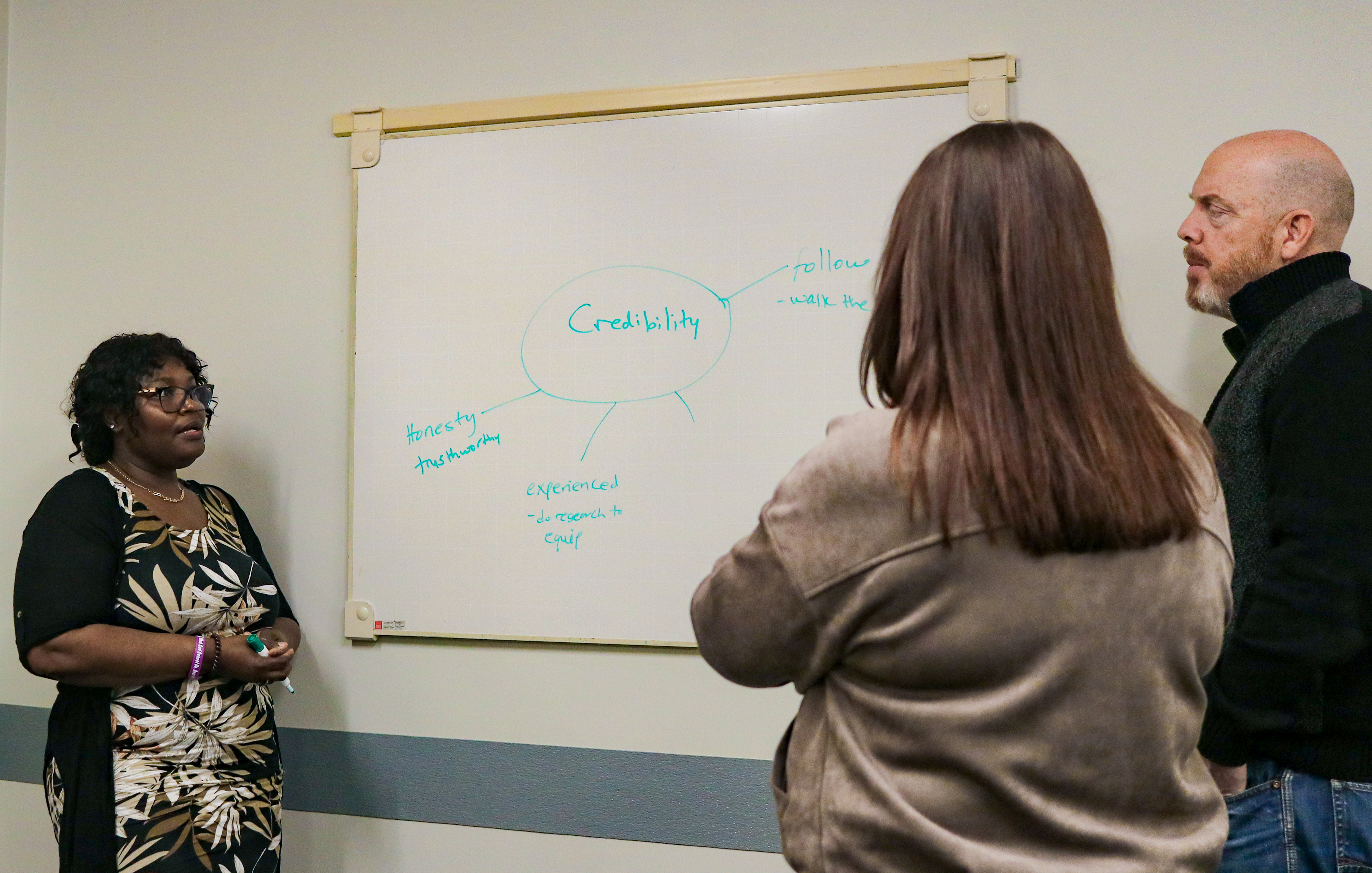 A woman talking and 2 people listening in a class
