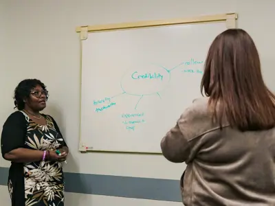 A woman talking and 2 people listening in a class