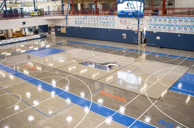 An empty multipurpose gymnasium with basketball hoops, court markings and Keyano Huskies championship banners.